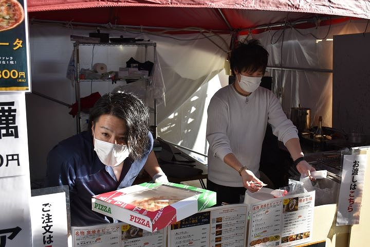 窯焼きピザを手に取って勧めるスタッフ
