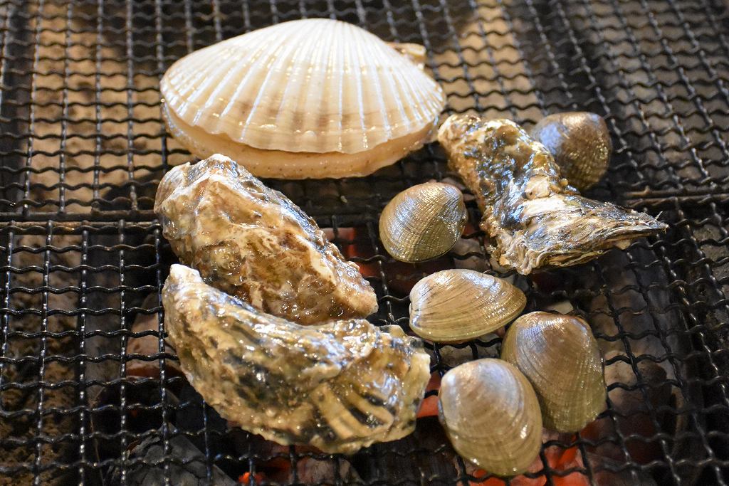 炭火の上の網で焼かれているホタテ、カキなどの魚介類
