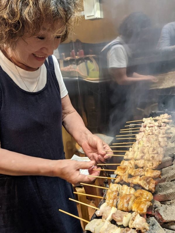 やきとりの焼き台の前に立つやきとり吉田屋の店主の吉田静枝さん