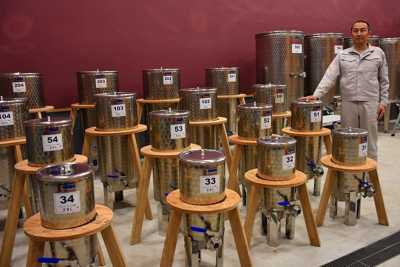 ずらりと並ぶ、生産者ごとに仕込まれた小型のタンクを前に立つ尾原基記さん