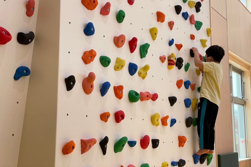 屋内交流施設ちゃいるもの遊戯広場にある突起をつかんで壁を登る遊具「クライミングウォール」で遊ぶ子供