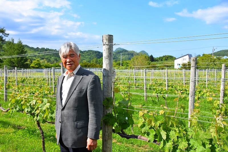 ブドウ畑をバックに笑顔を見せる「ワイナリー夢の森」代表の大下聡さん
