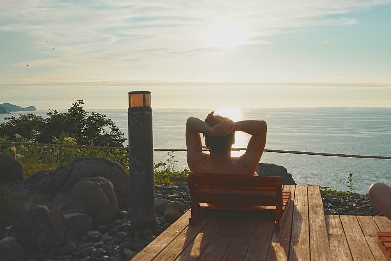露天風呂に新たに設けた「崖っぷちベンチ」で日本海の夕日を楽しむ参加者