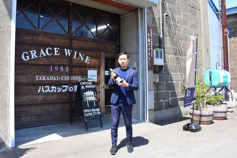 千歳ワイナリーの前でワインボトルを手にする社長の三澤計史さん