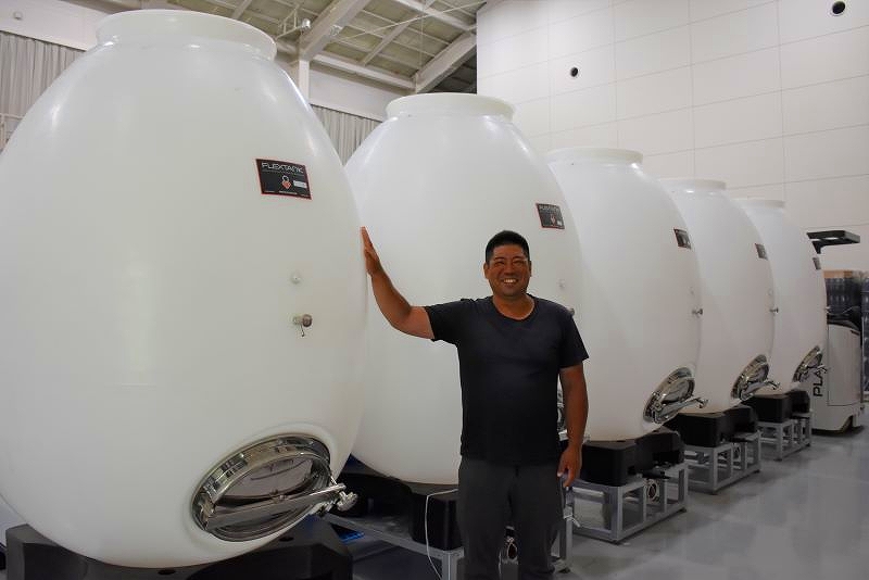 タンクの前で笑顔を見せる、栽培と醸造を担う東出和喜さん