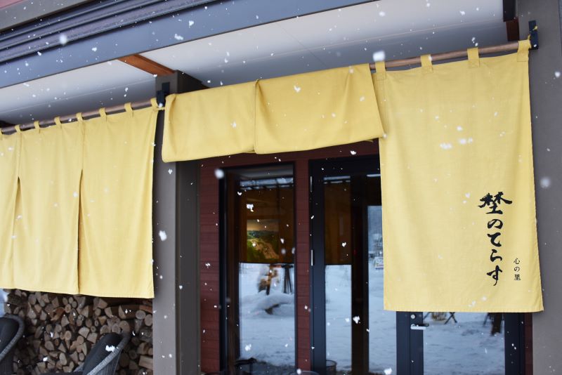 「心の里 埜(の)のてらす」の店舗入り口に掲げられた黄色いのれん
