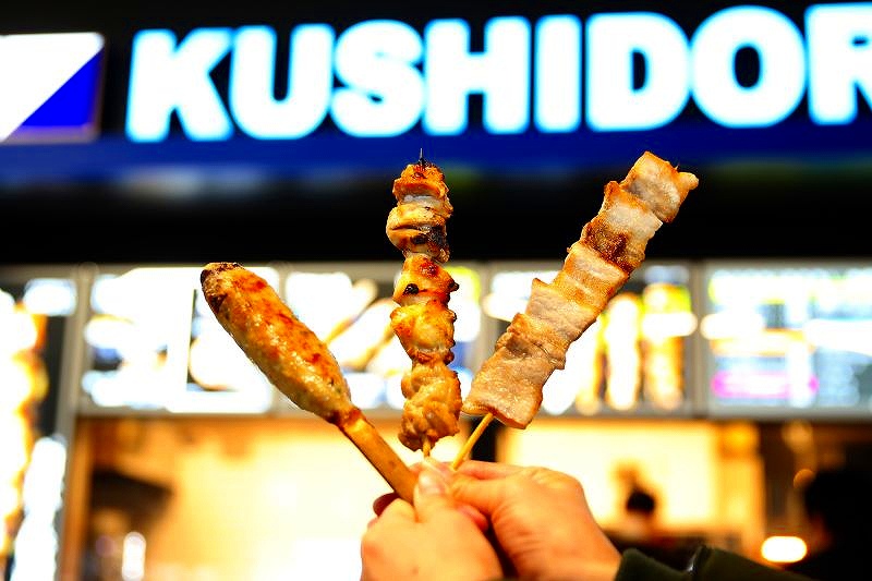 青い「串鳥」の看板の前で手にした商品の串３本