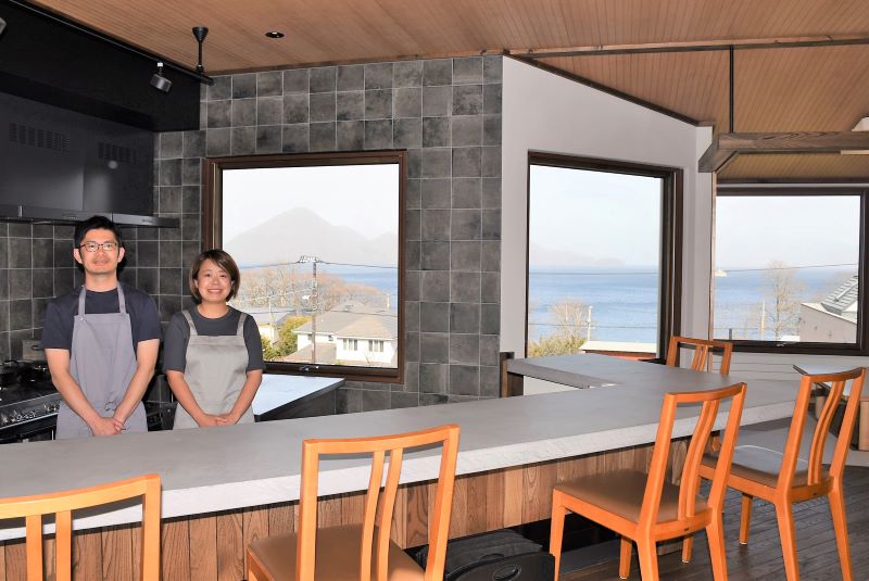 洞爺湖を望む「湖の膳舎なかむら」の店内で来店を呼び掛ける中村悠佑さん(左)と美佳さん夫妻