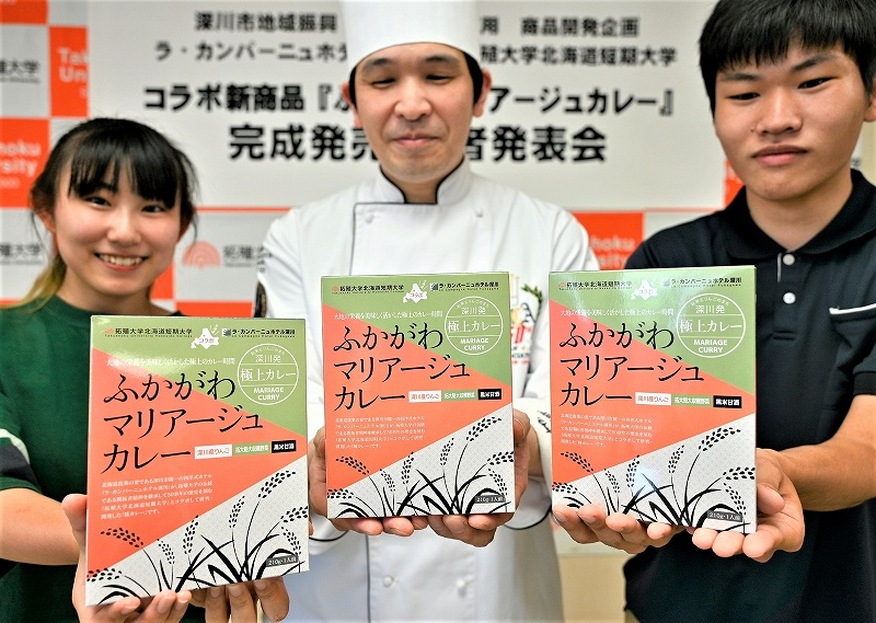 完成させたレトルトカレーを手にする林総料理長（中央）と開発担当の学生