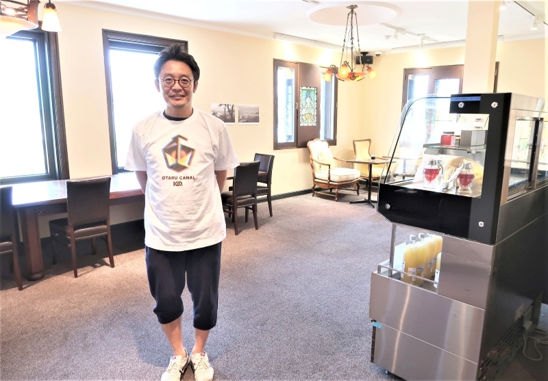 ミュージアムカフェを紹介する佐々木健二さん。窓の外は小樽運河が広がる