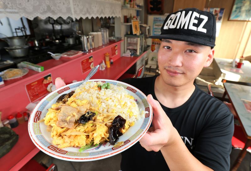 先代から受け継いだ名物のムースールー炒飯を手にする新店主の甲斐さん(藤井泰生撮影)