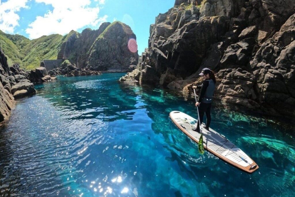 「奥尻ブルー」の上を、パドルをこいで水上を進むスタンドアップパドルボード(ゲストハウスimacoco提供)