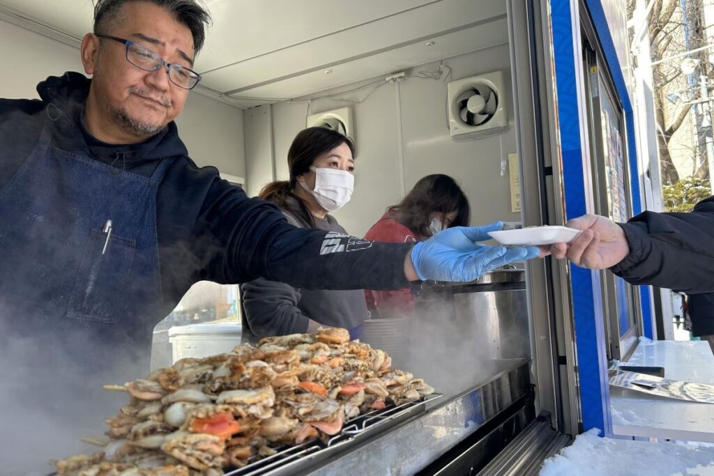 ホタテ串が湯気を上げる飲食ブースでのフードの受け渡しの様子