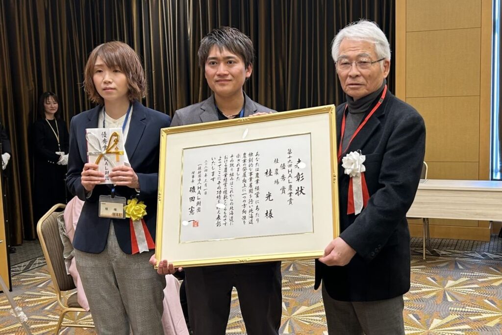 磯田理事長（右）から表彰状などを受け取った桂さん（中央）と妻〓さん