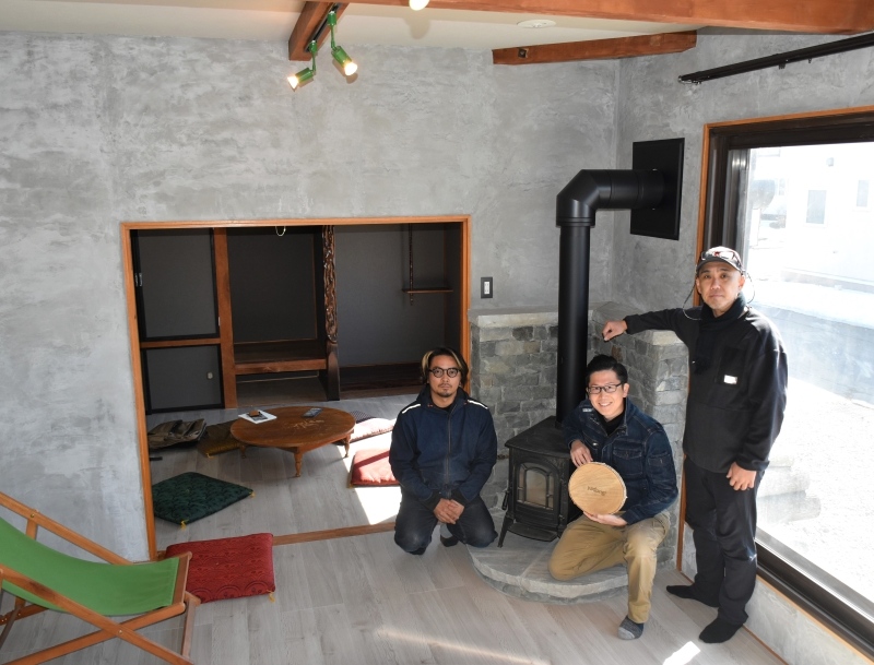 空き家をリフォームした民泊施設で、売りのまきストーブの前でＰＲする川瀬千尋さん（中央）ら