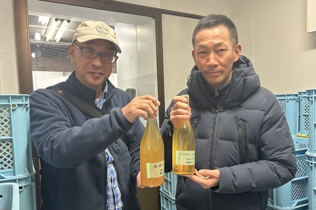 2023年のブドウでつくった旅路を手にする山口さん（左）とナイアガラを持つ福光さん