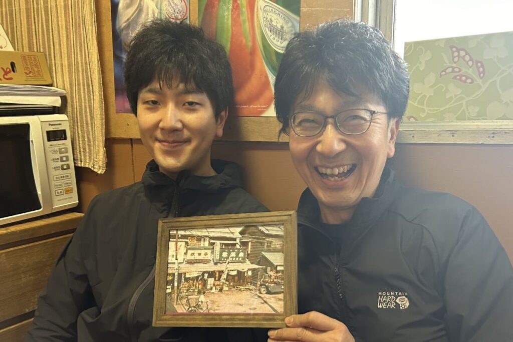 戦後まもなくの杉原商店の写真を手にする杉原社長(右)と一成店長