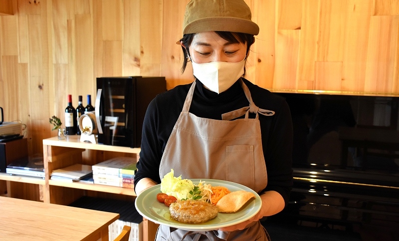 壁や床に木材を貼り、内装にもこだわった店内で、自家製のひき肉を使った「あらびきハンバーグ」を手にしている様子。