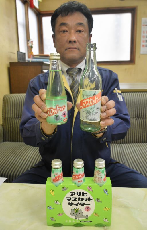 製造50周年を迎えた「マスカットサイダー」を手にするアサヒ飲料の桑田社長。左が現在の瓶で、右は発売当初の瓶