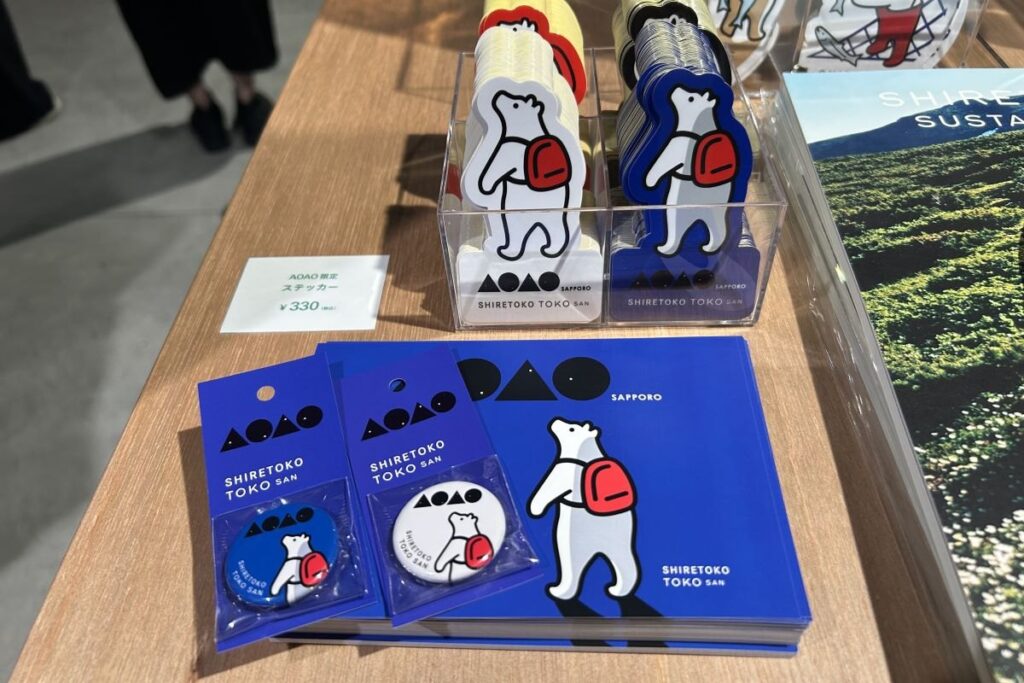 「知床トコさん」のAOAOオリジナル缶バッジ(手前左)やポストカード(同右)、ステッカー