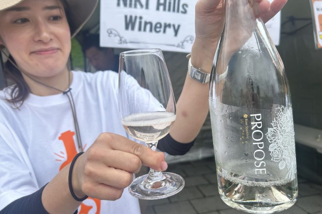 ニキヒルズワイナリーの「PROPOSE ROSE Sparkling(NV)」のボトルとグラスを手にするスタッフ